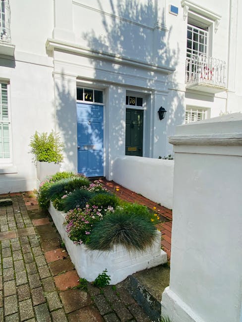A narrow front garden on Clapham Road SW9 featuring a trimmed lawn with neatly edged grass, bordered by a variety of plants and low hedge trimming. The garden bed showcases dark, moist soil with fresh